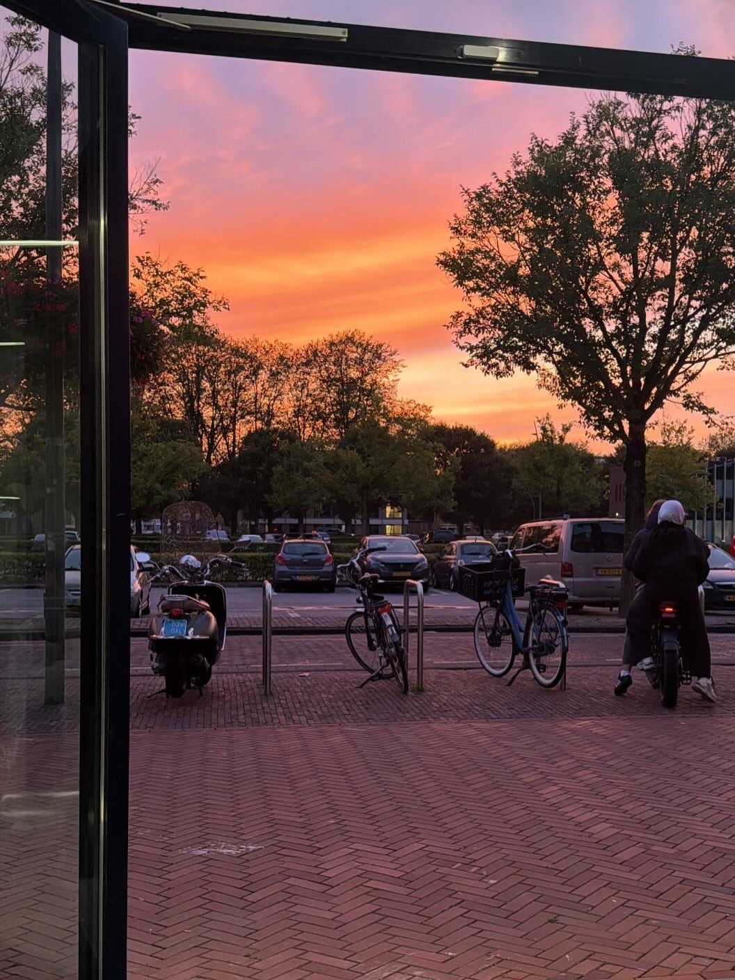 Uitzicht door de open deur van de zaak op de Schans bij zonsondergang, met fietsen op de stoep