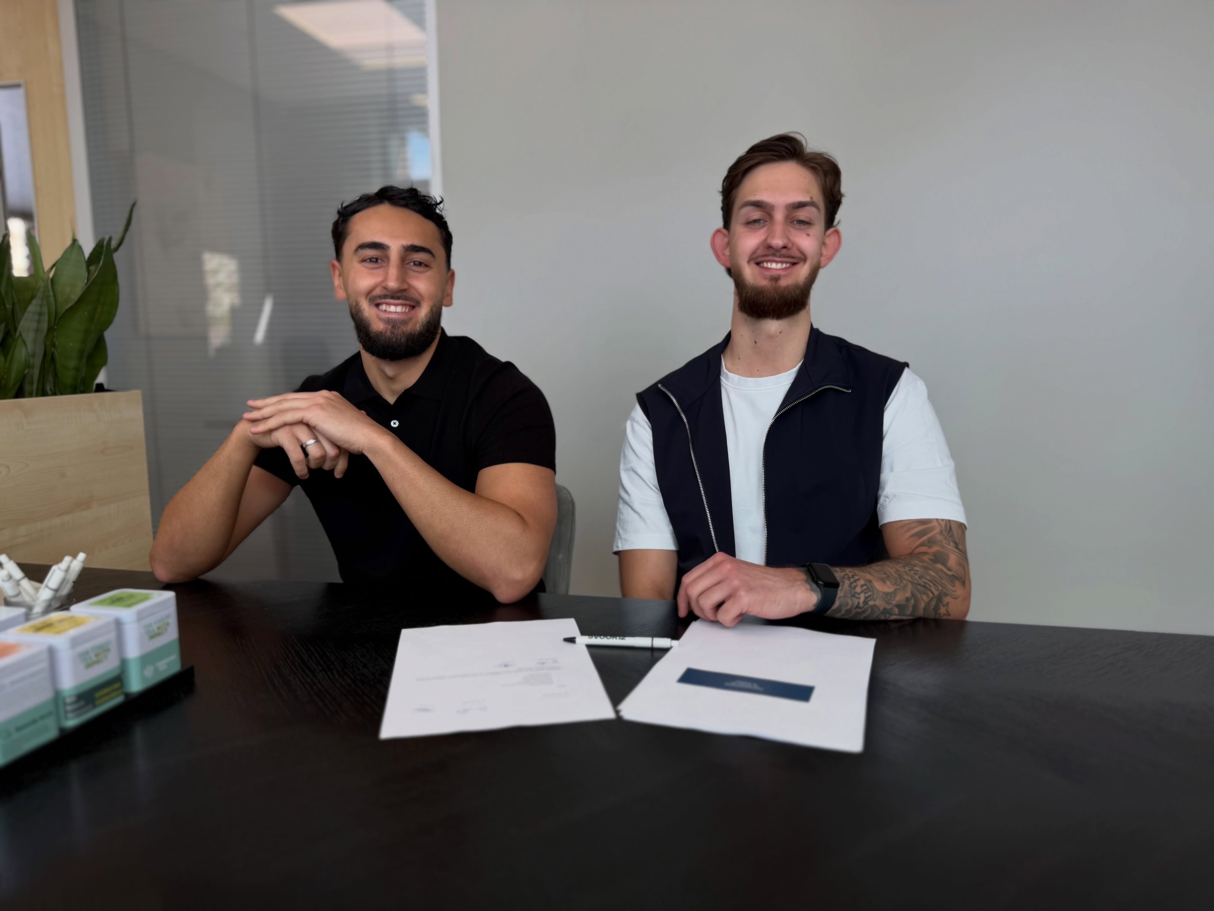 Twee barbers van het Nexus-team lachend aan een tafel met papieren